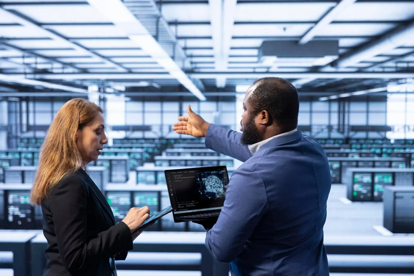 Команда техников в центре обработки данных, использующая ноутбук для визуализации ИИ.